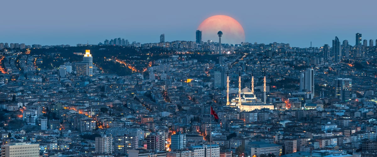 A cityscape with a prominent mosque and a large crescent moon in the sky.