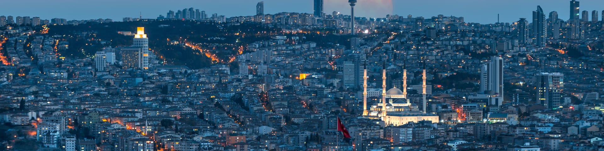 A cityscape with a prominent mosque and a large crescent moon in the sky.