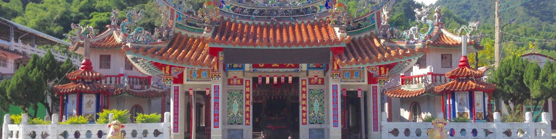 A traditional Chinese temple with ornate architecture and a lush green mountain backdrop.
