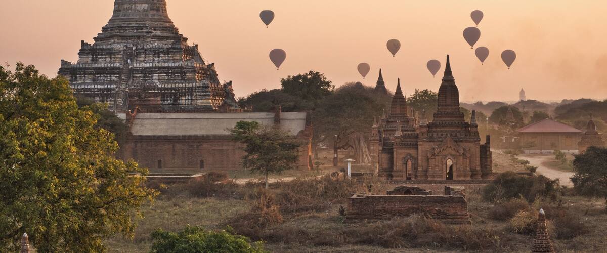 A temple complex with multiple structures, surrounded by trees and open fields.