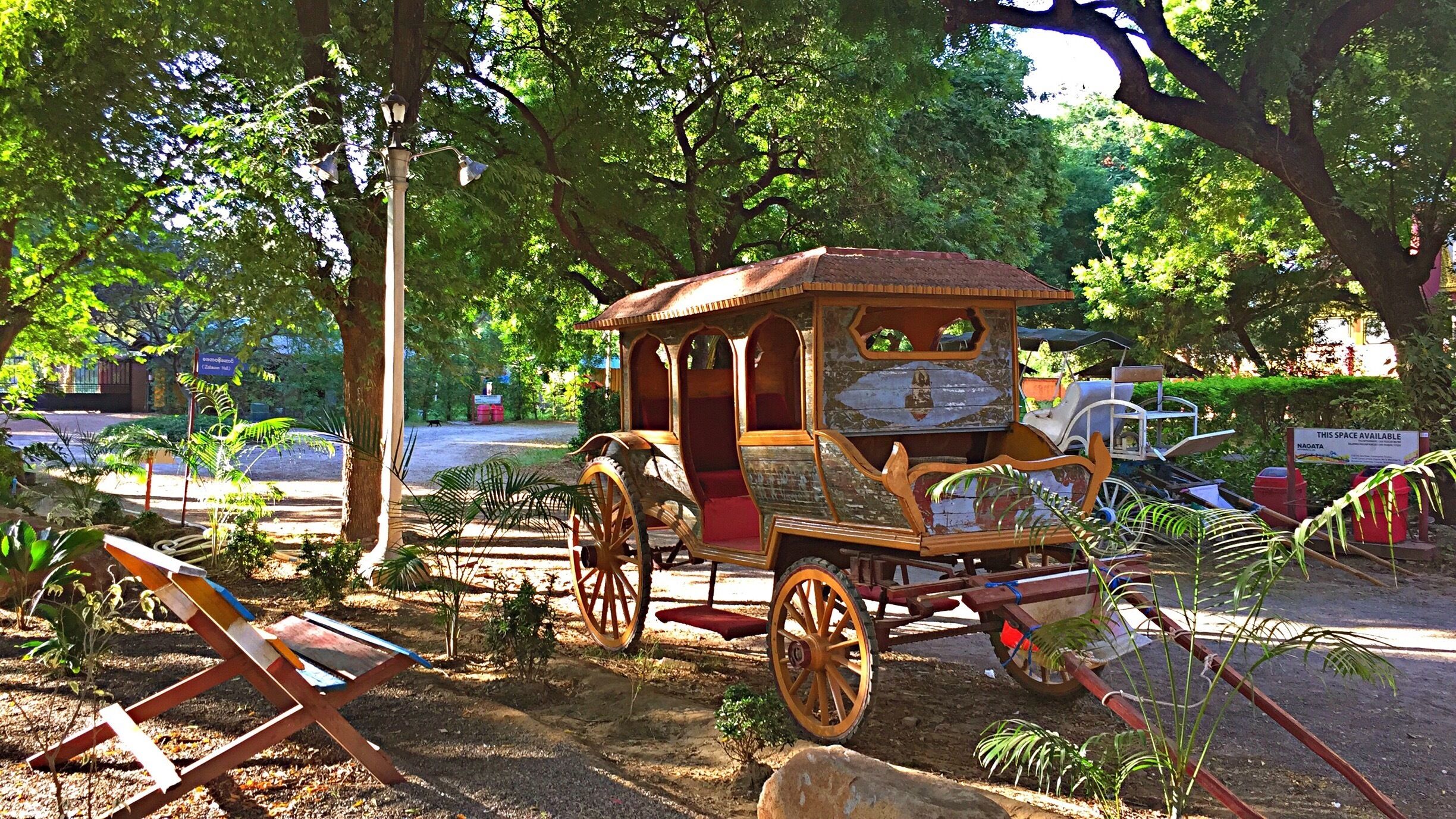 Un antiguo carruaje de madera con interior rojo, rodeado de árboles y plantas.