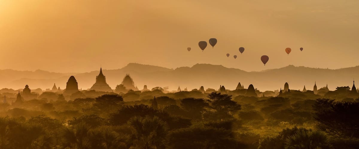 A landscape with temples and hot air balloons during sunset.