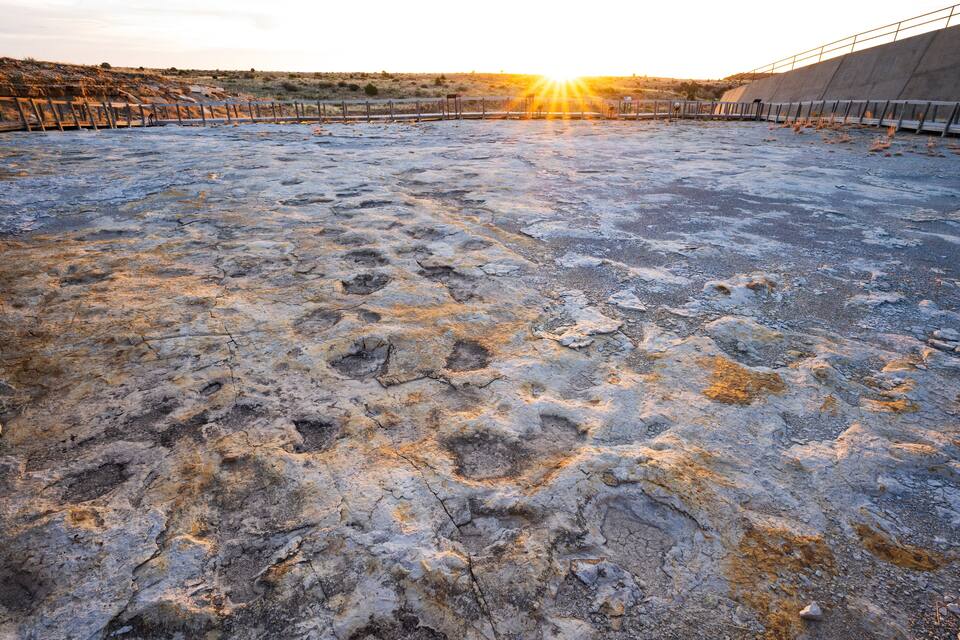 A rocky terrain with footprints and a concrete structure in the background.