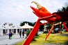 A large red crab sculpture in a public square with people walking around and a white building in the background.