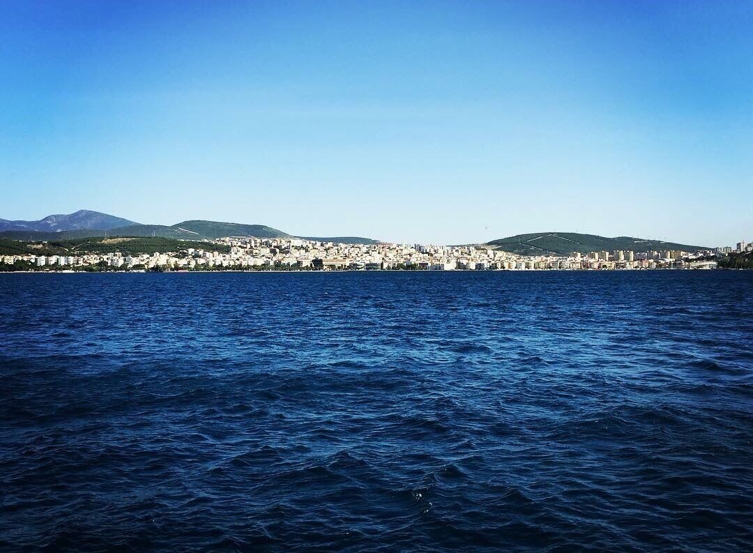 A coastal cityscape with a clear view of the sea and distant hills.