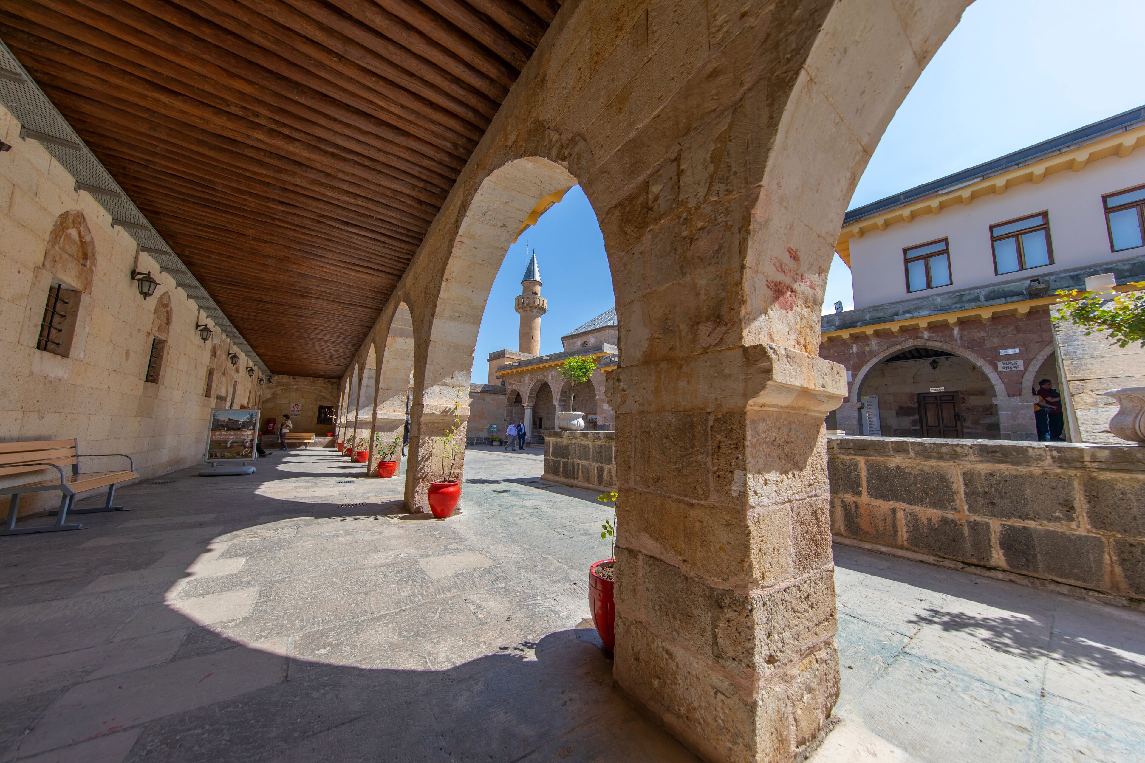 An open courtyard with stone arches, a wooden ceiling, and potted plants.