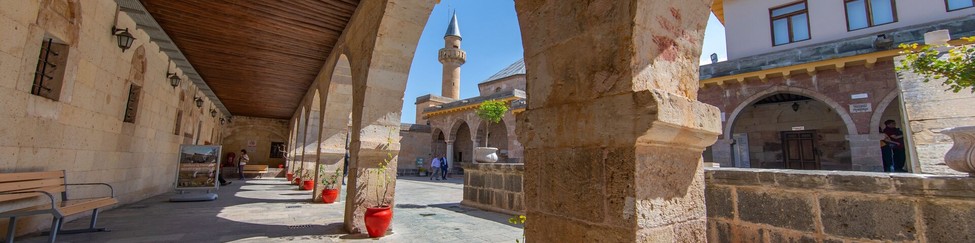An open courtyard with stone arches, a wooden ceiling, and potted plants.