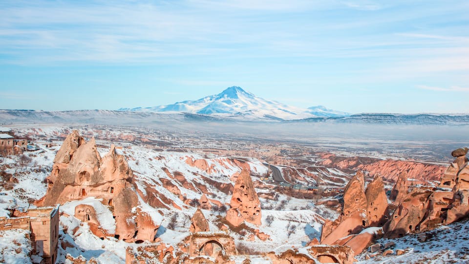 A snow-covered mountain with unique rock formations in the foreground.