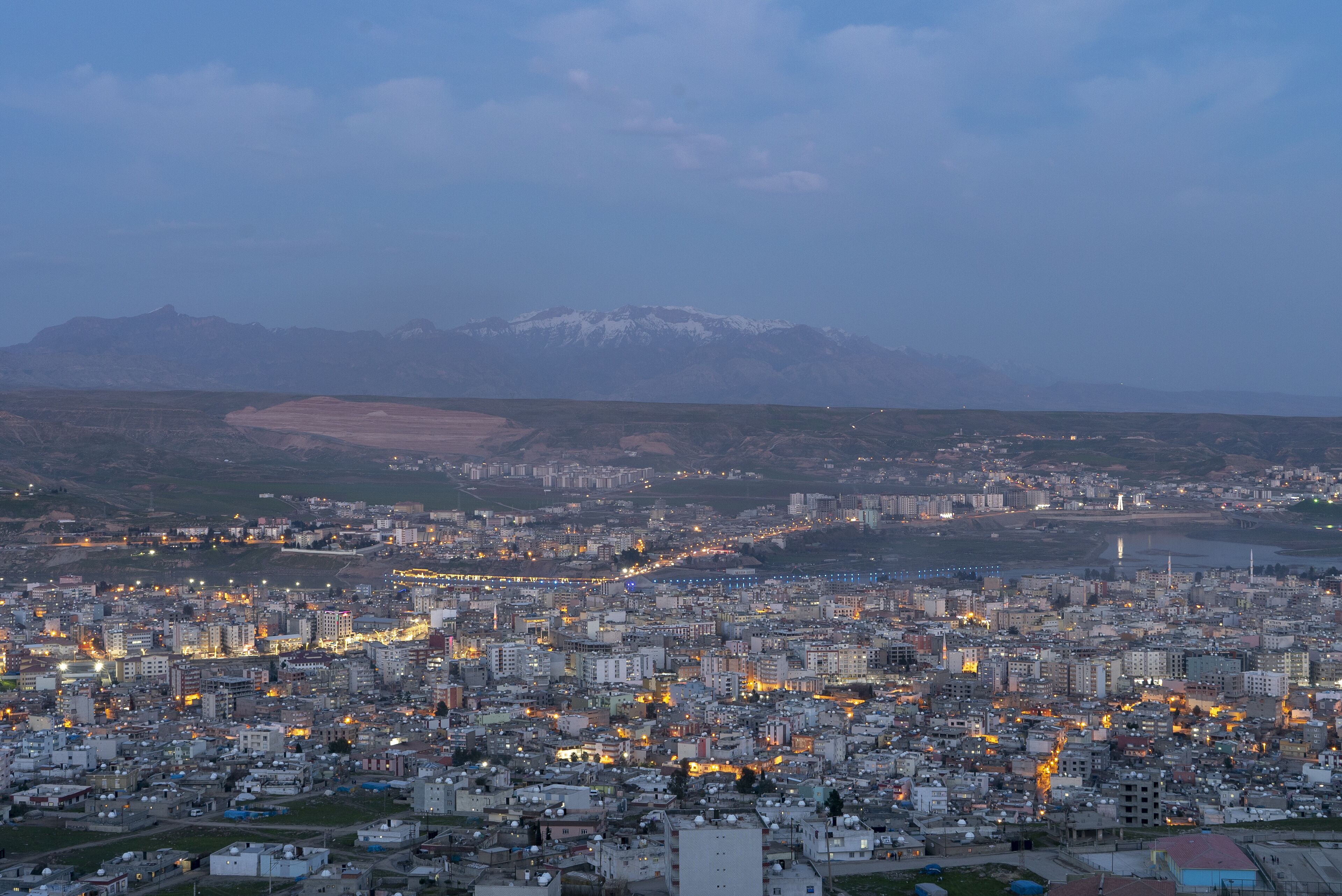 Un paisaje urbano al anochecer con una cadena montañosa al fondo.