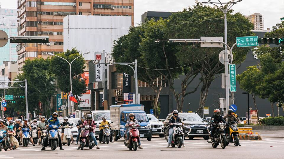 Una concurrida calle urbana con varios motociclistas, automóviles y peatones.