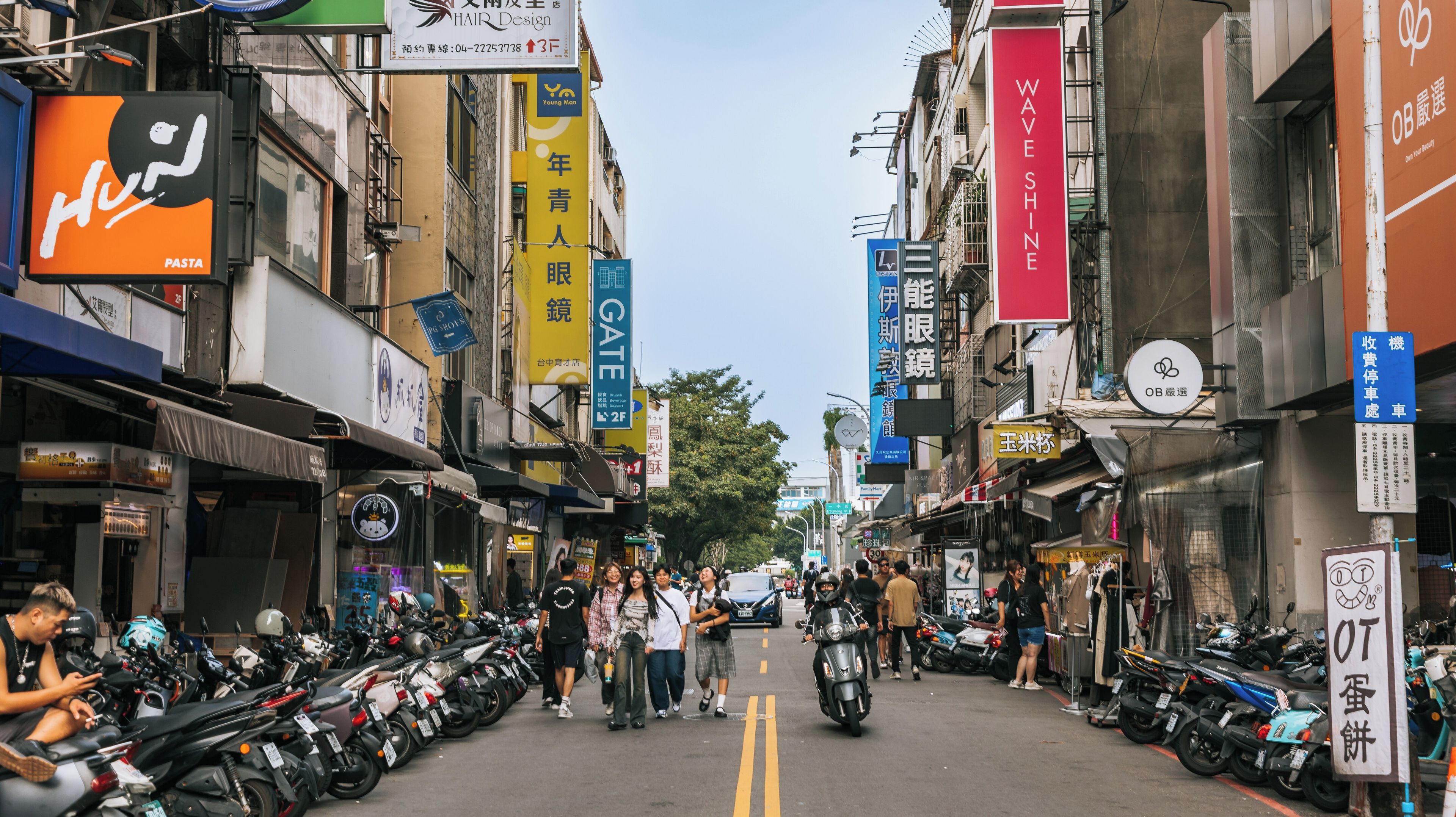 A busy urban street lined with shops and motorcycles parked on the side.