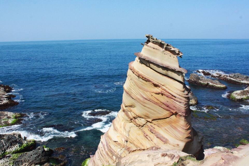A coastal rock formation with layered sedimentary structures and the ocean in the background.