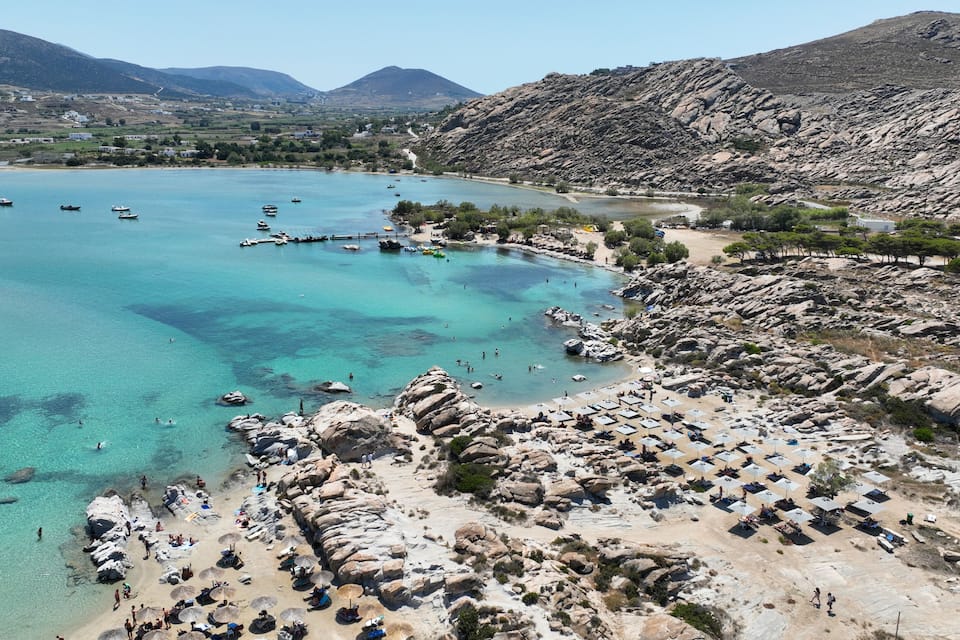 A coastal area with clear turquoise waters, rocky beaches, and a mountainous backdrop.