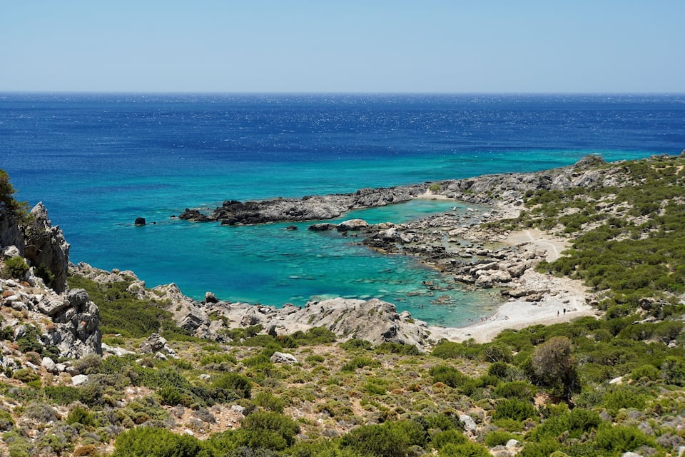 Eine Küstenlandschaft mit türkisfarbenem Wasser, felsigem Gelände und vereinzelter Vegetation.