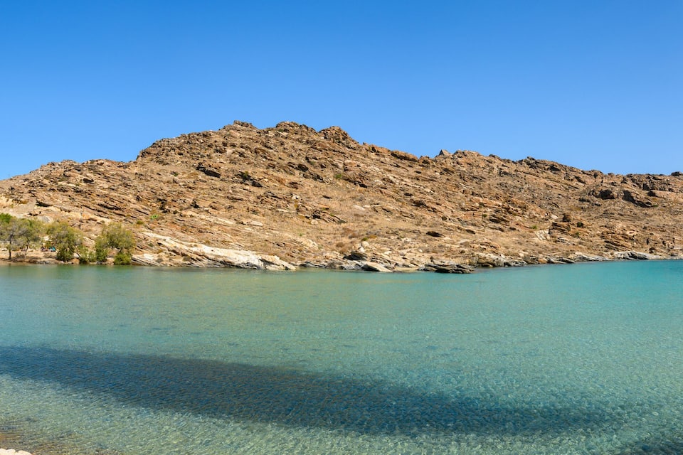 Ein felsiges Gebirge, klares türkisblaues Wasser und ein Strand mit Sonnenschirmen.