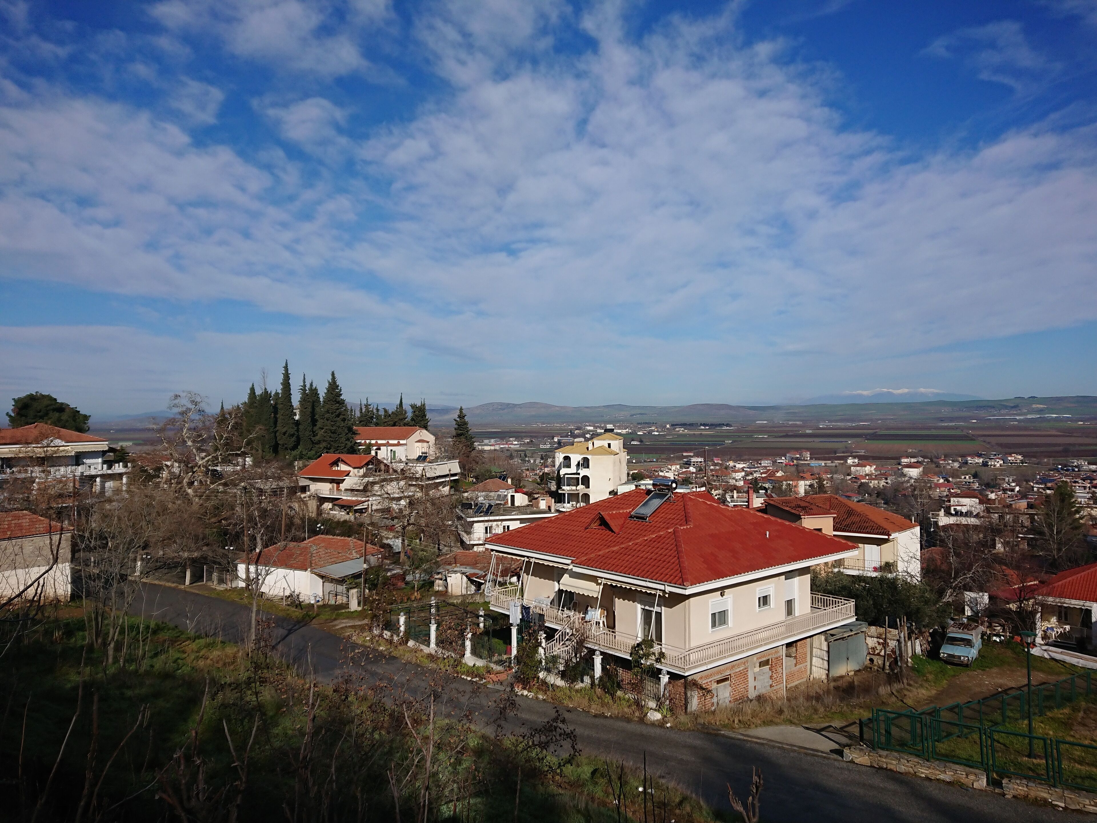 A residential area with red-roofed houses, a church, and a view of distant mountains.
