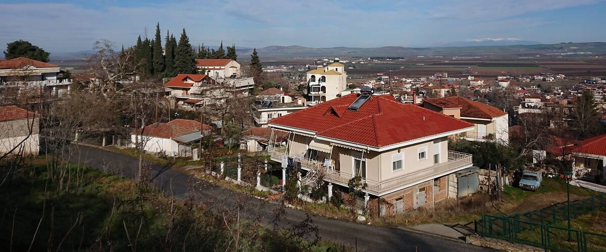A residential area with red-roofed houses, a church, and a view of distant mountains.
