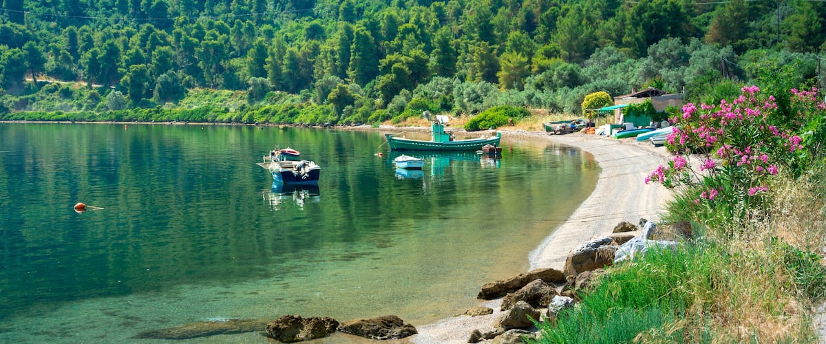 A serene lake with boats, a sandy beach, and lush green hills in the background.