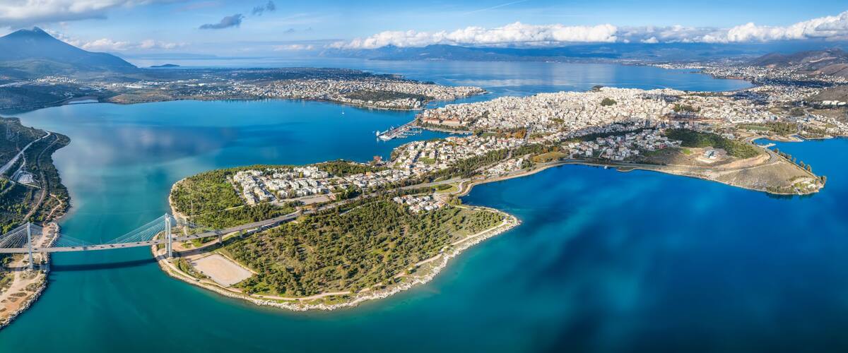 An aerial view of a coastal city with a prominent bridge, a large body of water, and surrounding mountains.