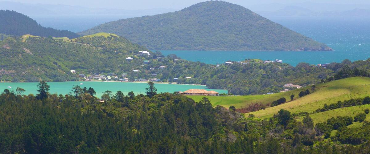 A coastal landscape with a turquoise bay, green hills, and scattered houses.