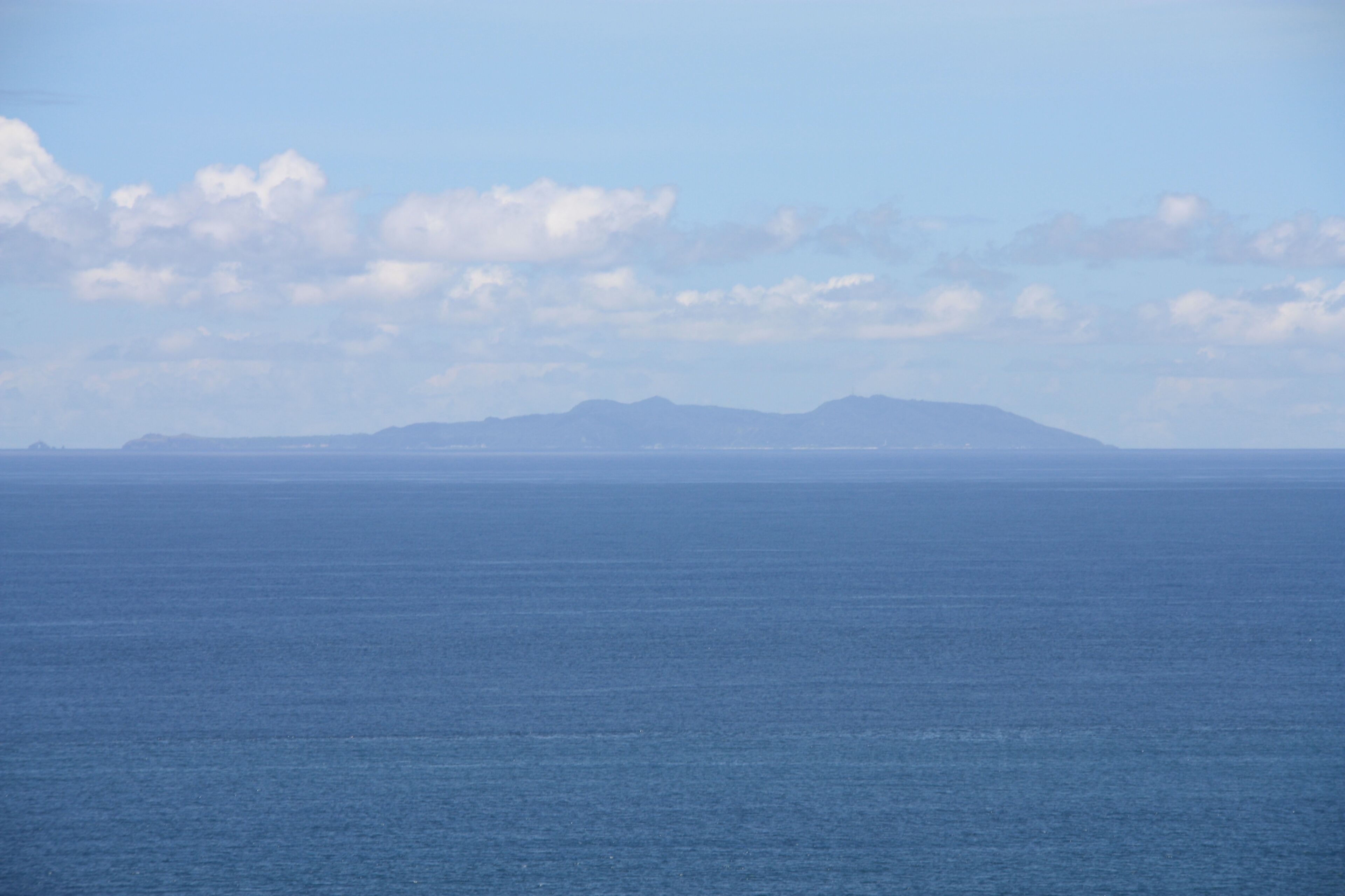 A calm sea with a distant mountain range under a partly cloudy sky.