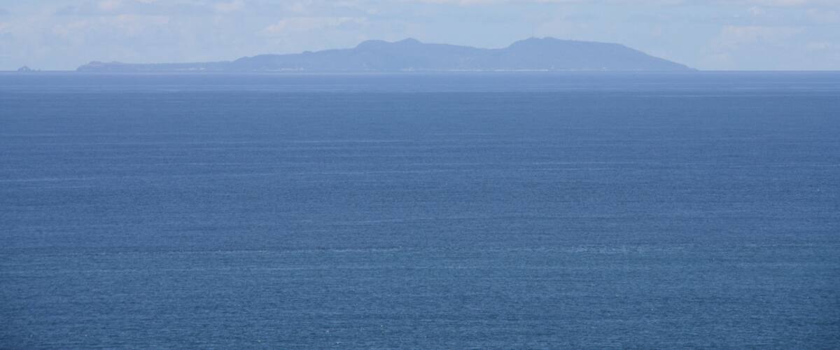A calm sea with a distant mountain range under a partly cloudy sky.