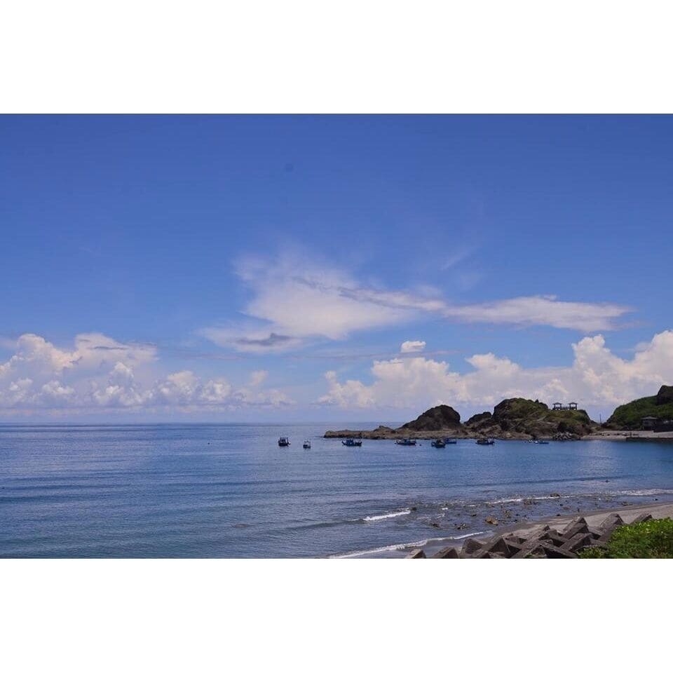 A coastal landscape with calm blue waters, rocky outcrops, and a clear sky.