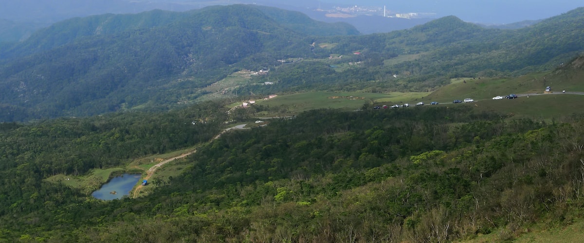 A mountainous landscape with a lake, a road, and distant buildings.