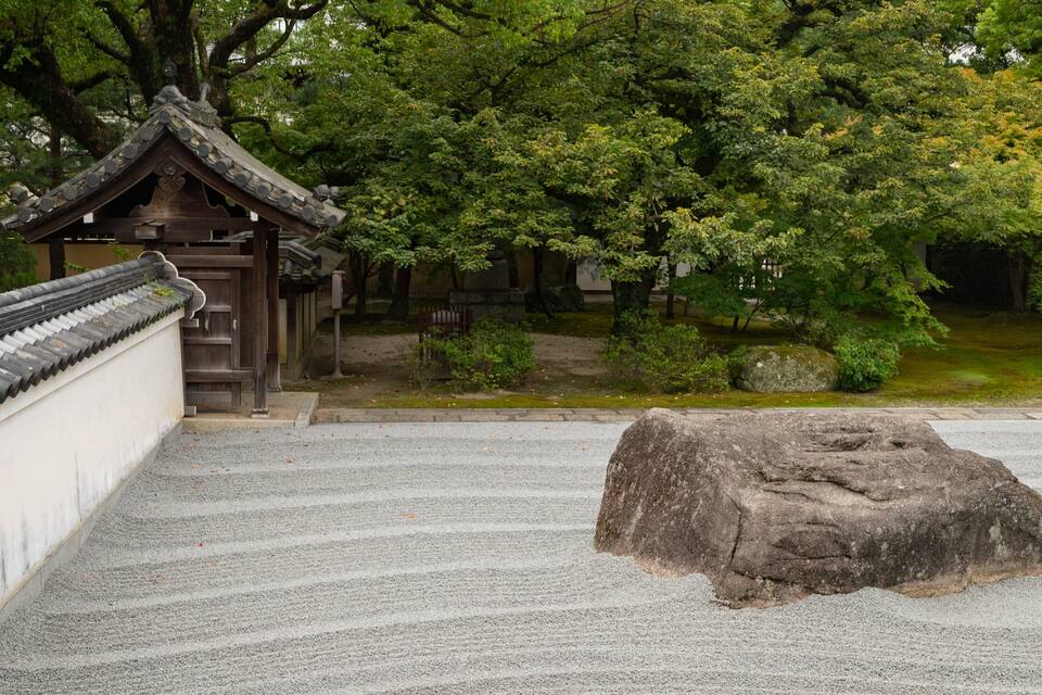 A traditional Japanese temple with a tiled roof, surrounded by lush greenery and a stone lantern.