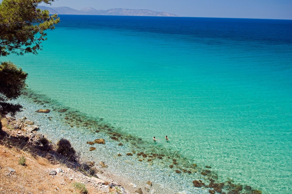 A clear turquoise sea with rocky shorelines and distant mountains.