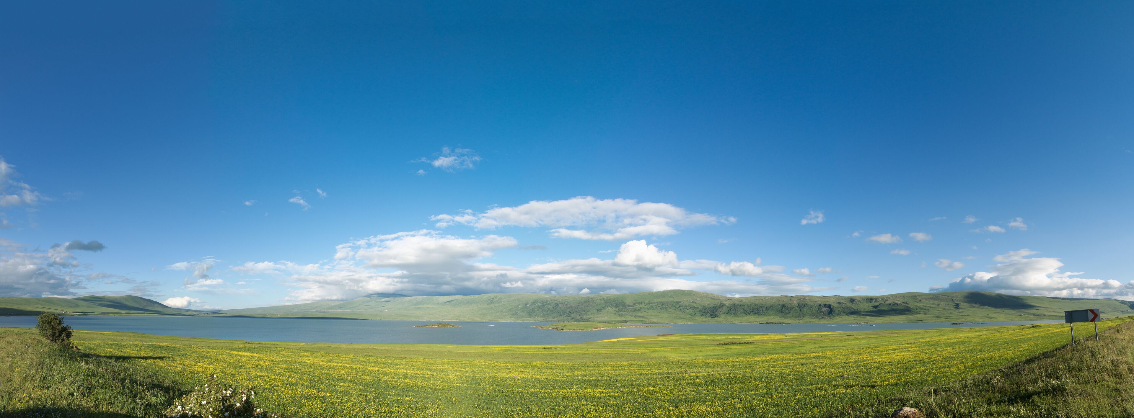 A lake surrounded by green fields and hills under a clear blue sky.