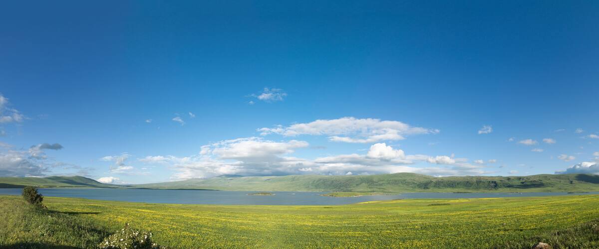 A lake surrounded by green fields and hills under a clear blue sky.