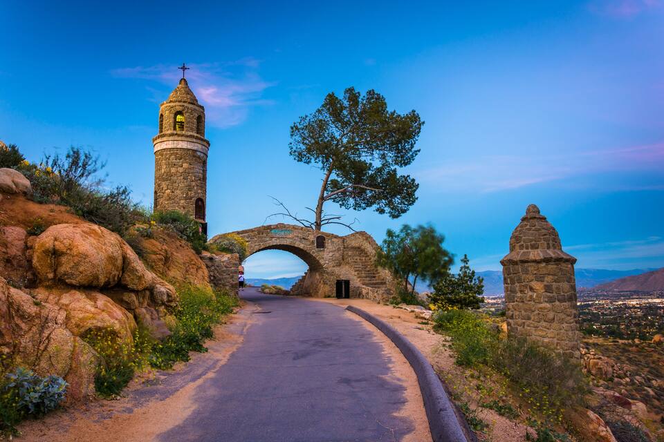 A stone archway, a bell tower, and a road leading through a mountainous landscape.