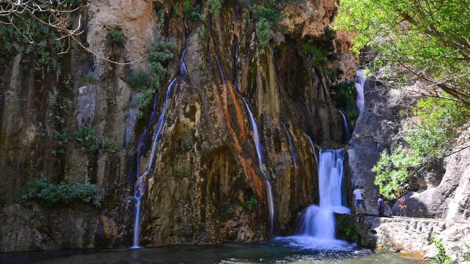 A waterfall cascading down a rocky cliff surrounded by lush greenery.