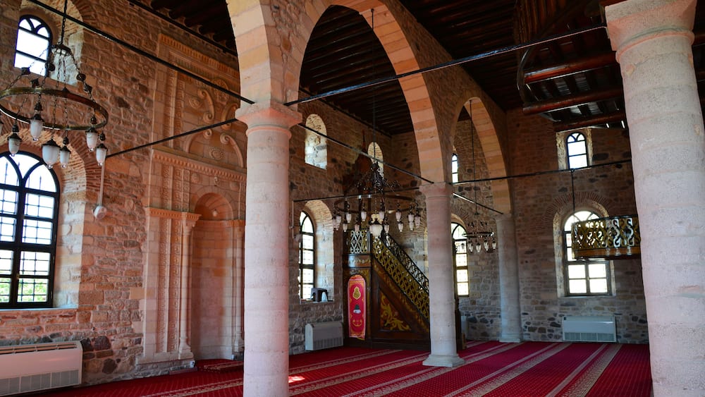 Un intérieur caractérisé par des arches en pierre, une moquette rouge et un escalier orné de balustrades travaillées.