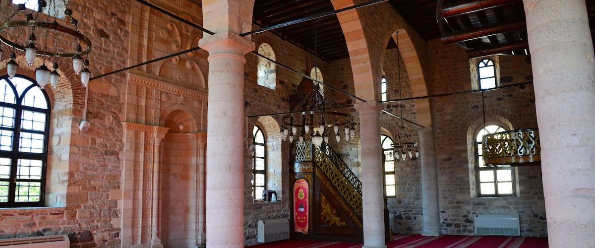 An interior with stone arches, a red carpet, and a staircase with ornate railings.