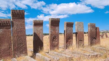 Ancient stone pillars with inscriptions in a dry grass field under a clear blue sky.