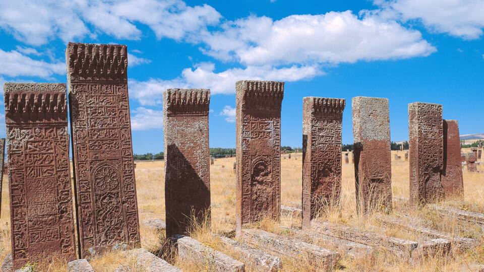 Ancient stone pillars with inscriptions in a dry grass field under a clear blue sky.