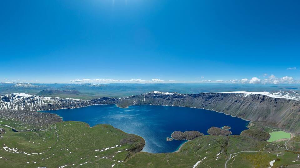 A large crater lake surrounded by mountains and snow-covered peaks.