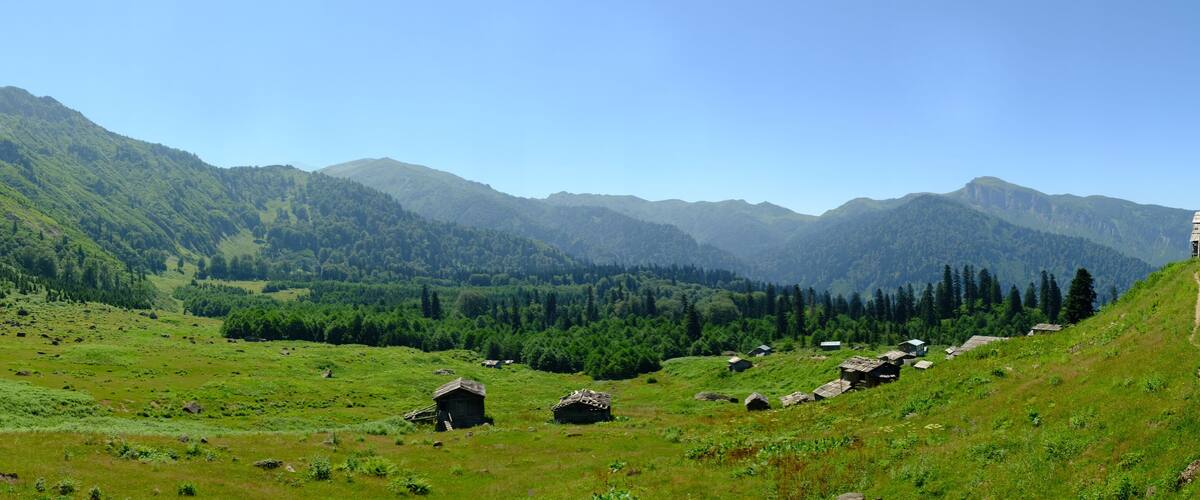 A mountainous landscape with green fields, scattered rocks, and traditional wooden houses.