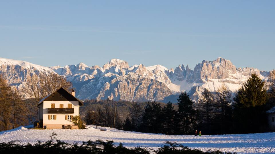 A snow-covered mountain range with a chalet in the foreground.