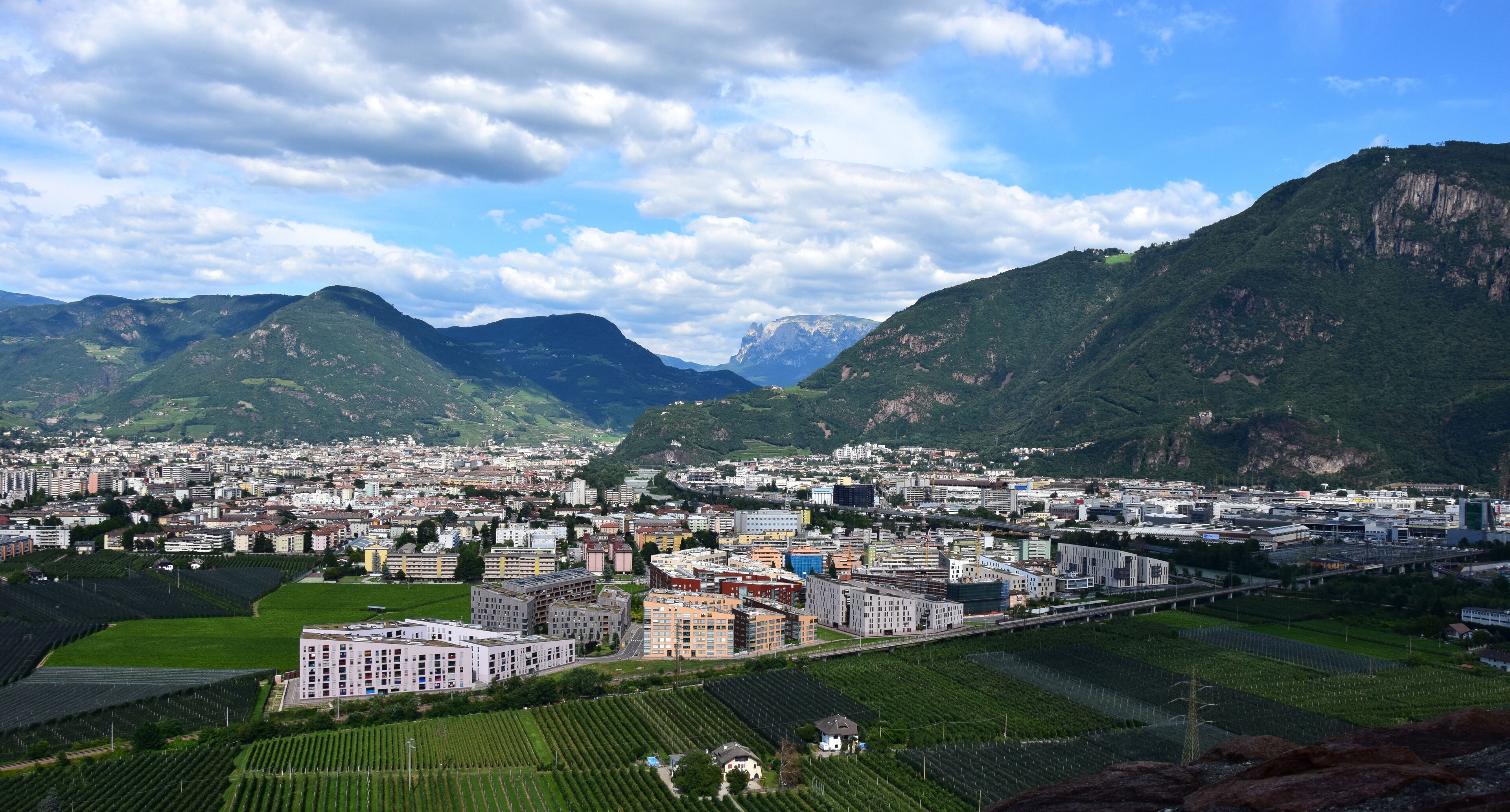 A cityscape with mountains in the background, a bridge, and agricultural fields.