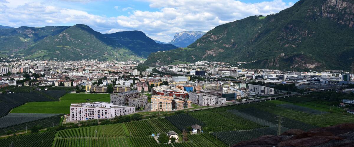 A cityscape with mountains in the background, a bridge, and agricultural fields.