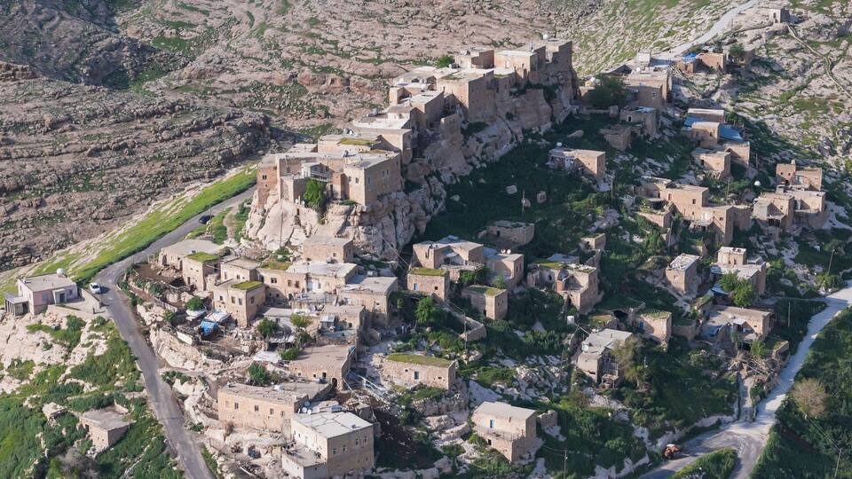 A rugged mountainous village with stone buildings and a prominent castle-like structure.