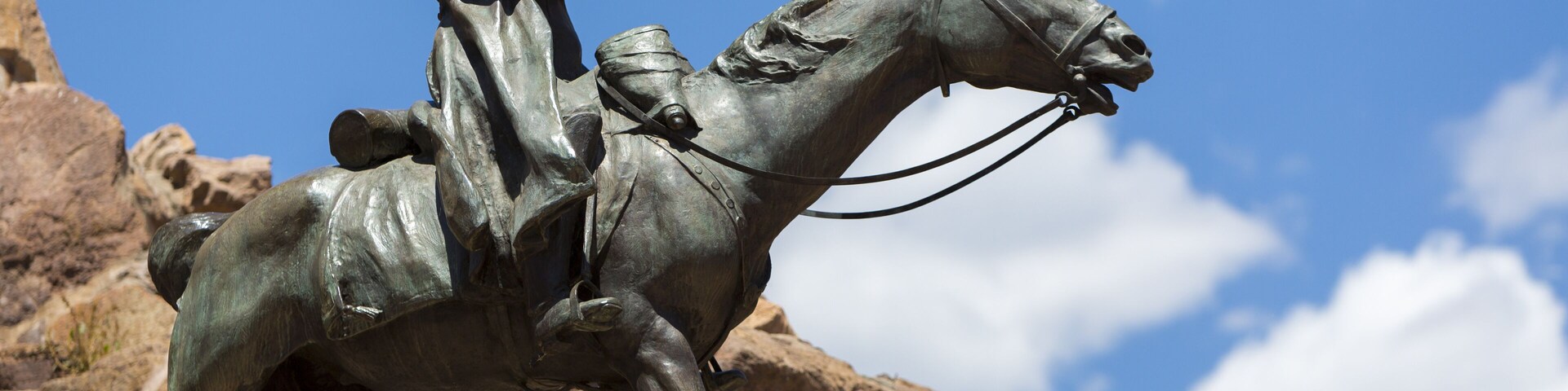Una estatua de bronce muestra una figura a caballo, con un paisaje rocoso y un cielo azul despejado de fondo.