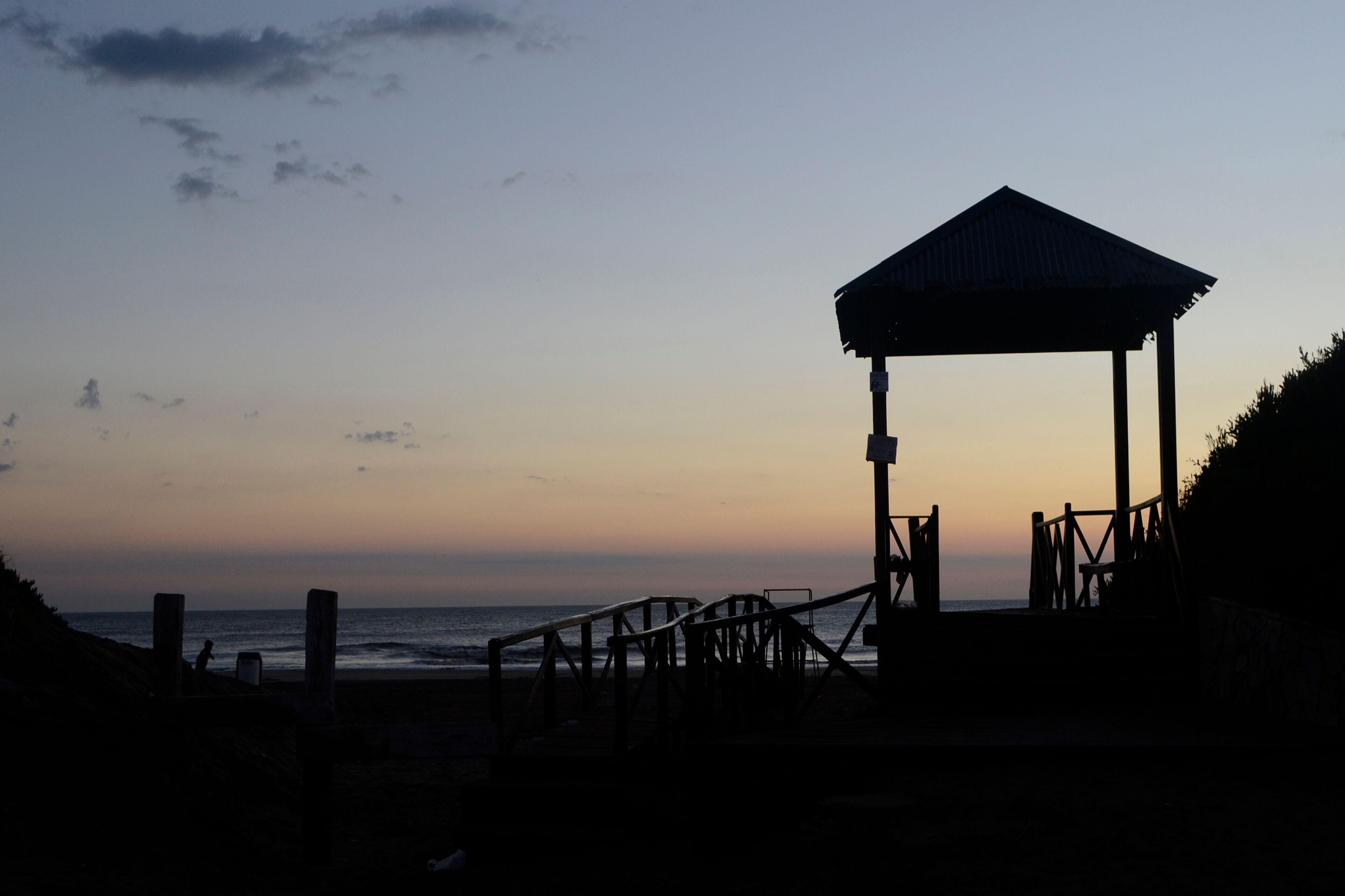 A beach with a wooden gazebo and a staircase leading to it.