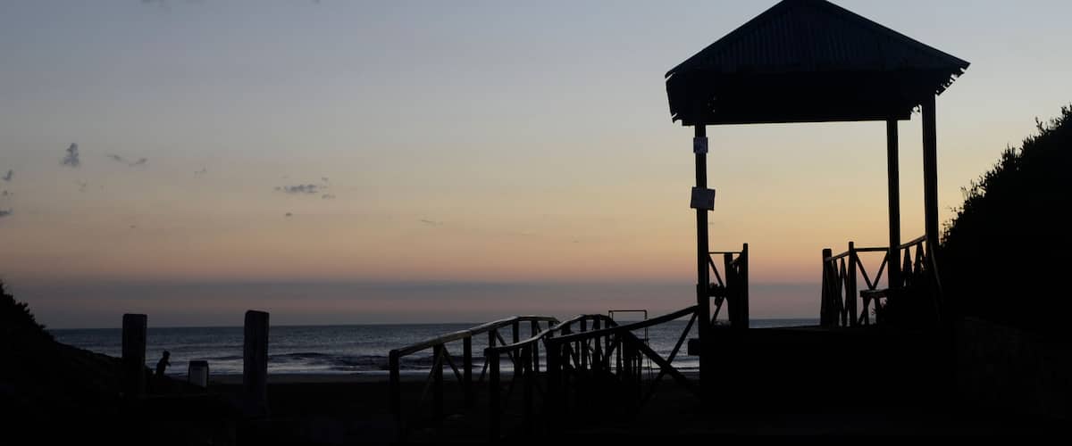 A beach with a wooden gazebo and a staircase leading to it.