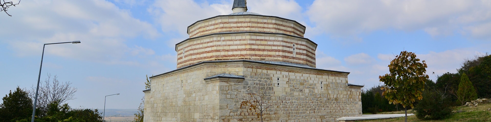 Un edificio histórico de piedra con una cúpula y aguja, rodeado de calles empedradas y vegetación.