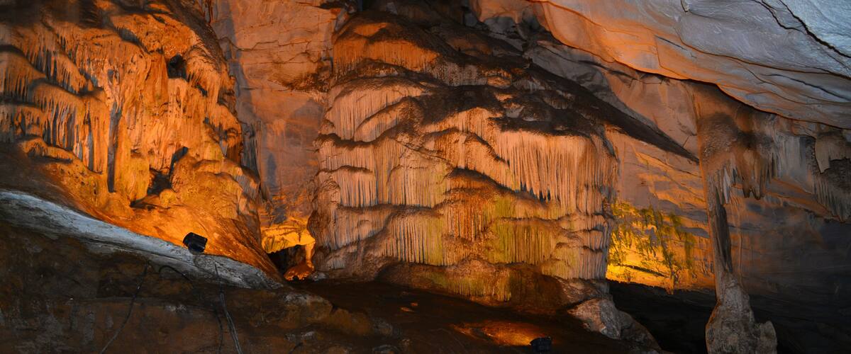A cave with stalactites and stalagmites, illuminated by artificial lighting.