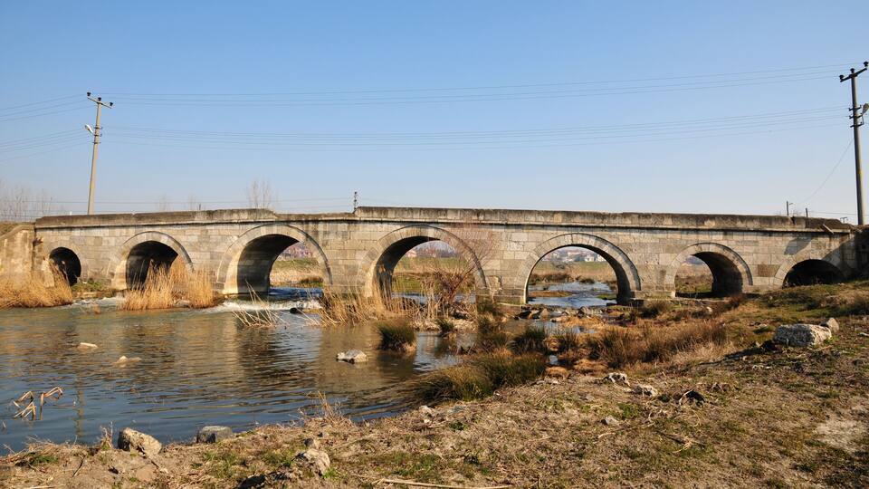 A stone bridge over a river with multiple arches and a clear sky.